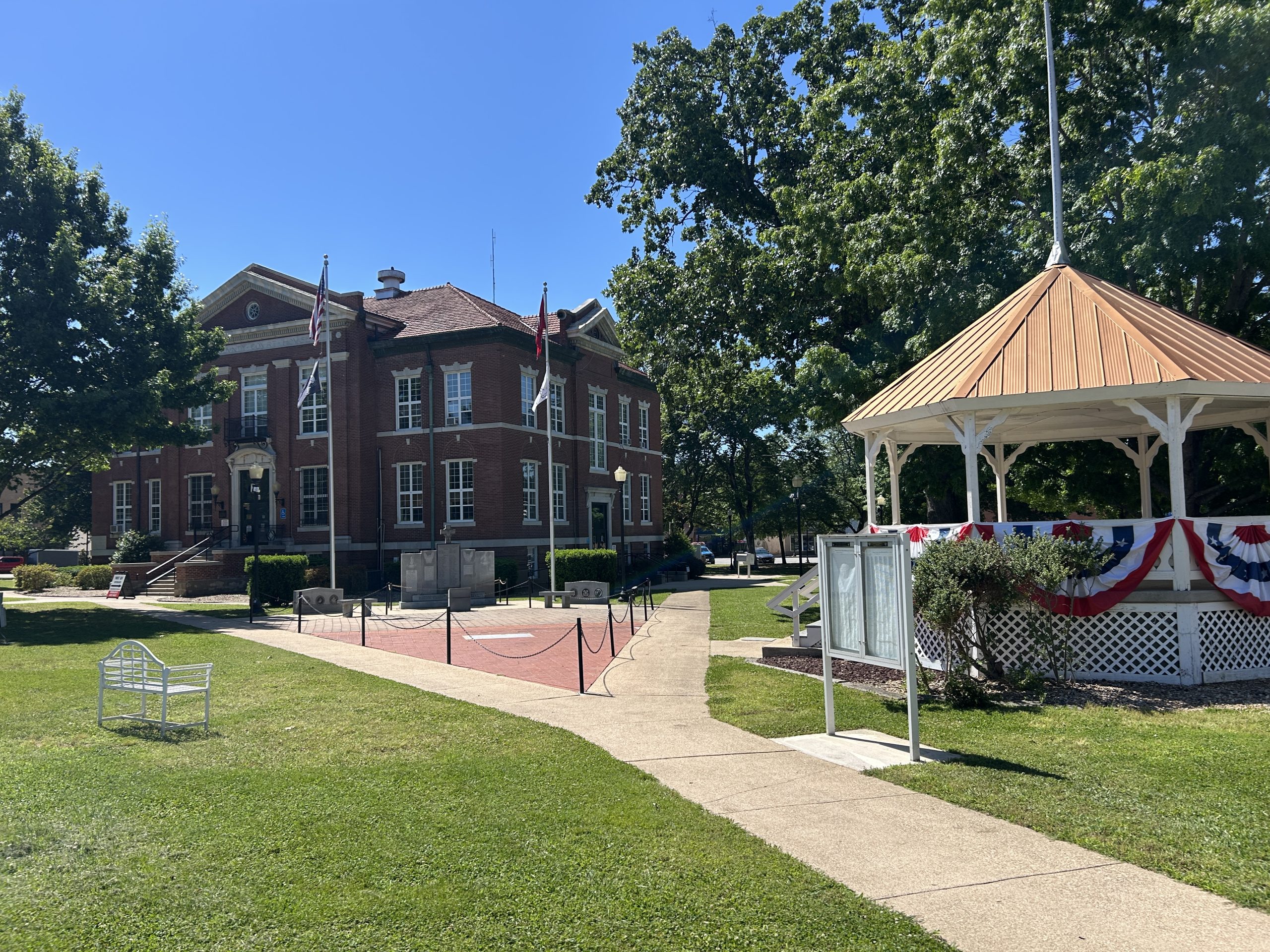 Historic courthouse and gazebo in downtown Harrison, Arkansas on a sunny day with green lawn, trees, and patriotic bunting.