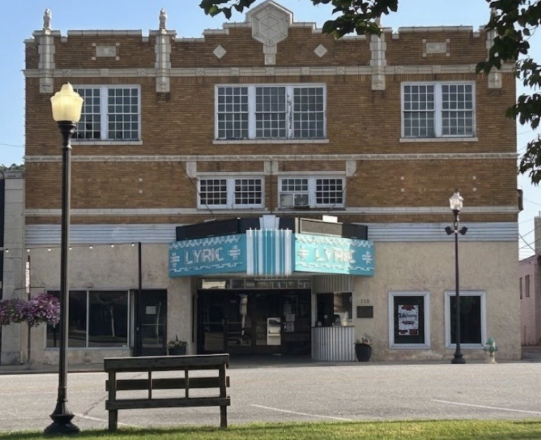 The historic Lyric Theater in downtown Harrison, Arkansas, viewed from across the street with its turquoise marquee, brick façade, bench, and streetlamps.